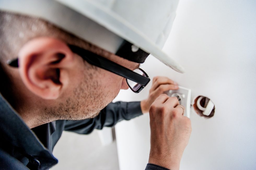 Electrician fixing a wall outlet on a white wall.