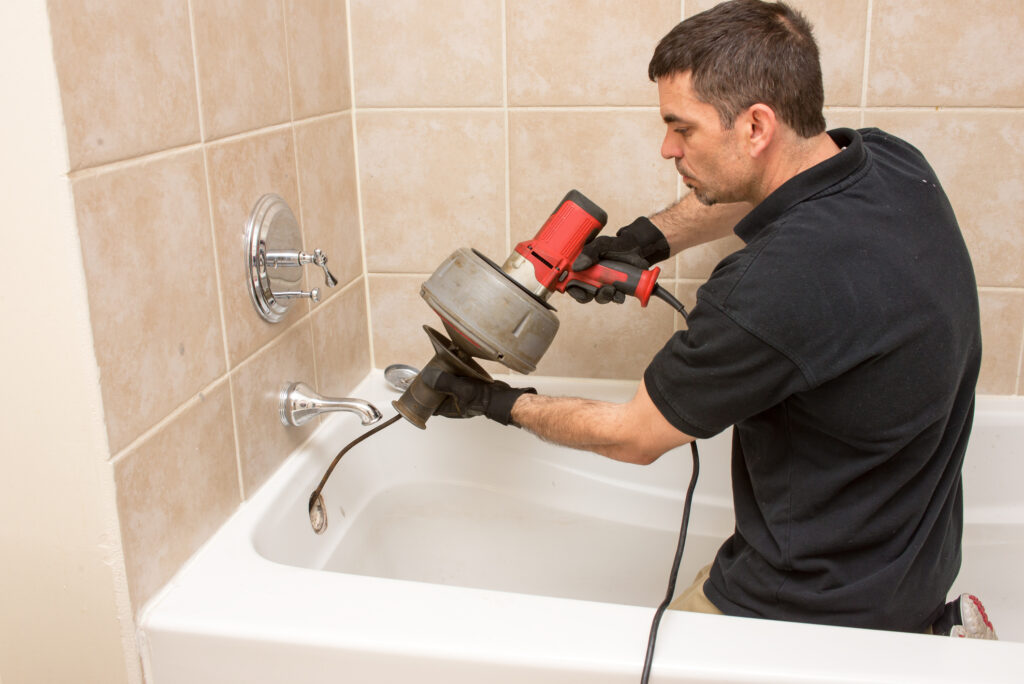 Plumber using power auger in tub drain