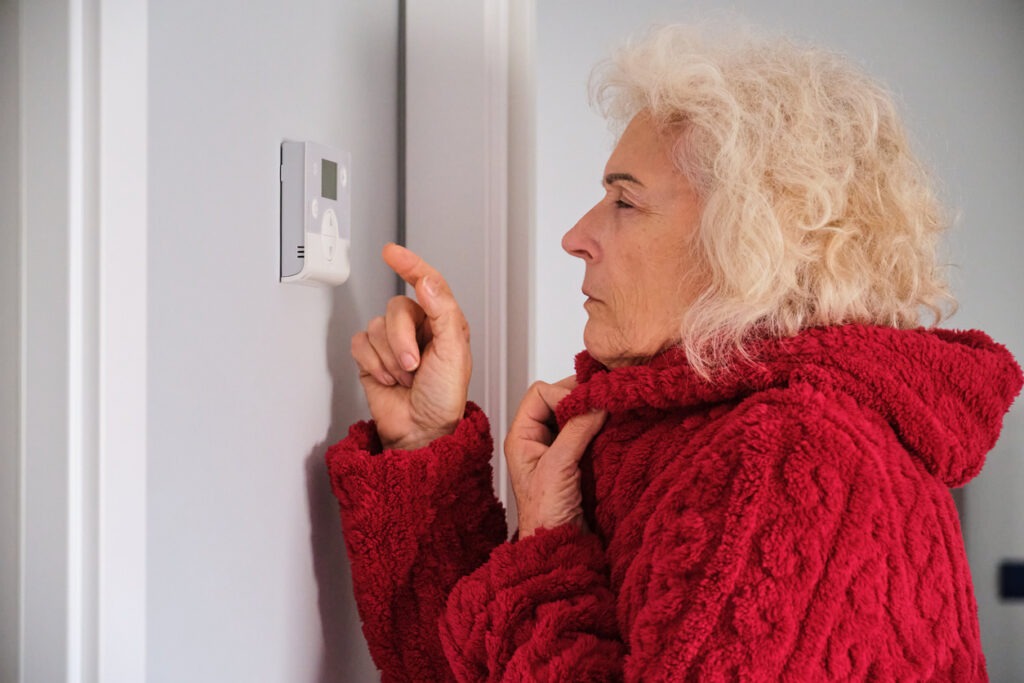 woman feeling cold in winter at home adjusting the thermostat