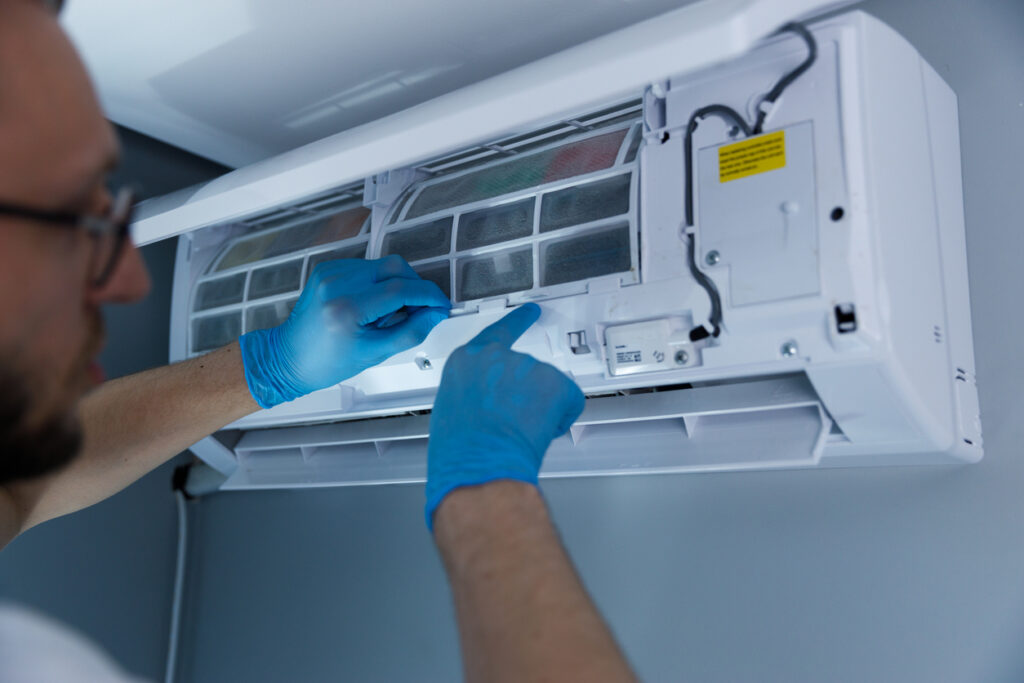 An experienced technician wearing blue gloves is inspecting and cleaning the filter of a split air conditioning unit on the wall, ensuring it operates efficiently in a home environment.
