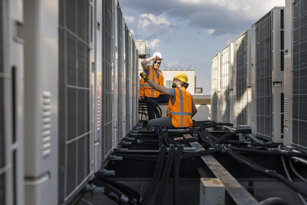 Rooftop air conditioning system inspection. Workers check units and log the result with a portable computer.
