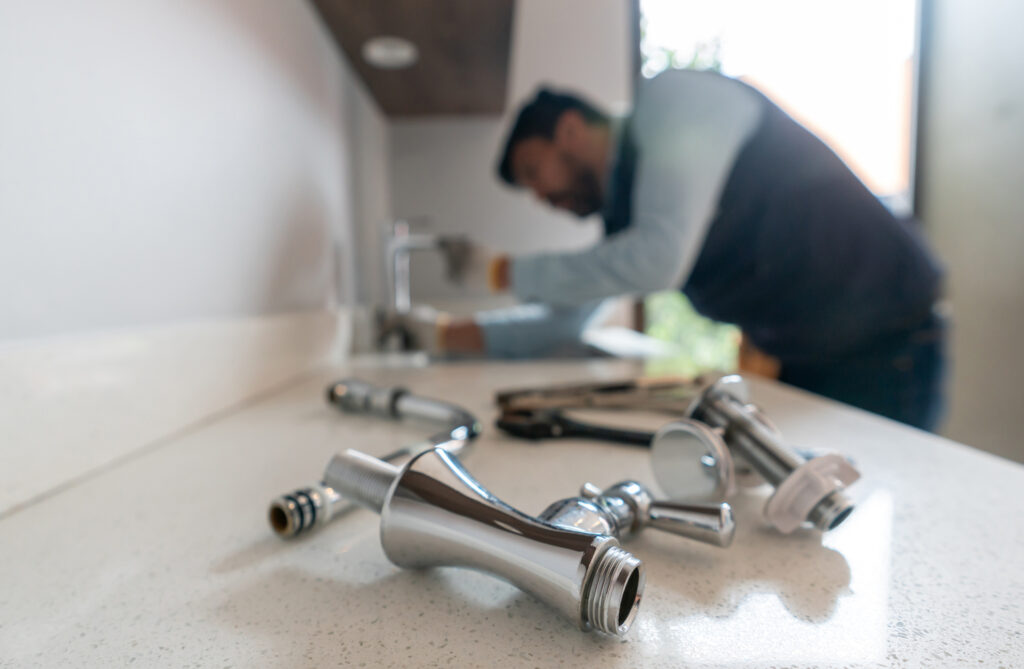 plumber fixing a leak in the kitchen sink of a house with focus on his tools