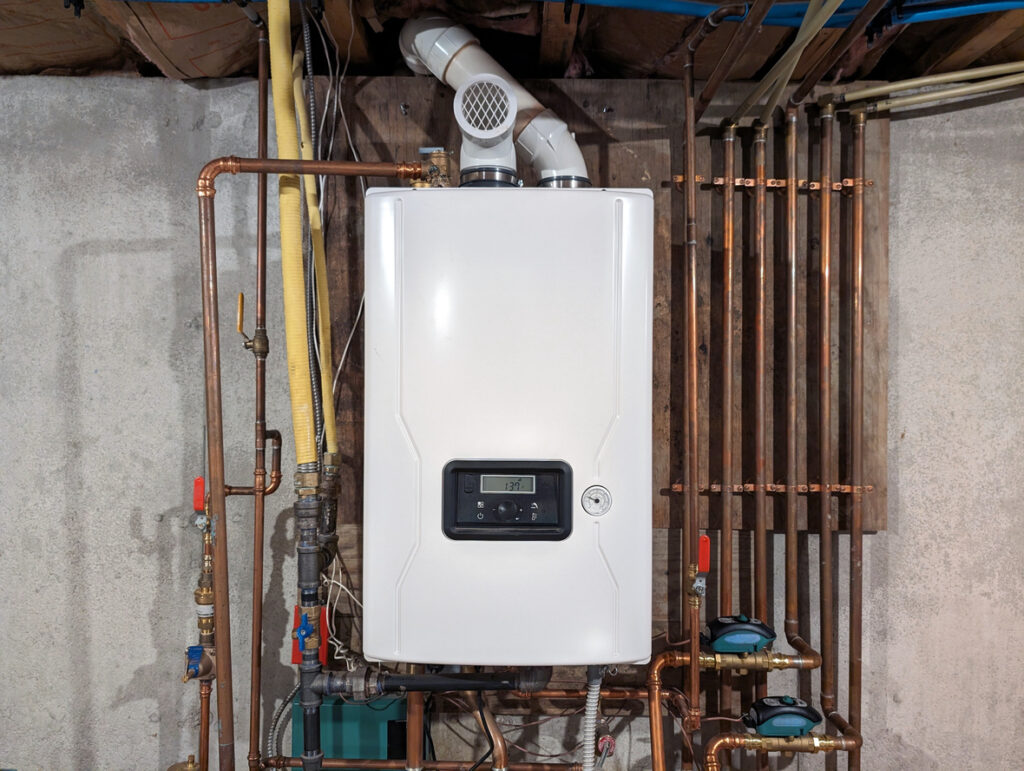Straight-on color shot of a Tankless Combination Water Heater installed on a well-lit basement wall of a home